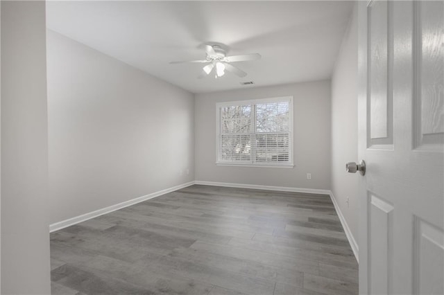 unfurnished room with ceiling fan, wood finished floors, visible vents, and baseboards