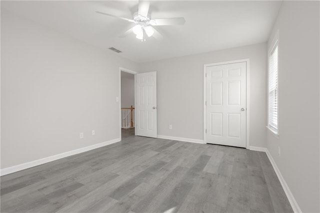 unfurnished bedroom featuring a ceiling fan, visible vents, baseboards, and wood finished floors