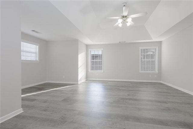 empty room featuring a raised ceiling, visible vents, a ceiling fan, wood finished floors, and baseboards