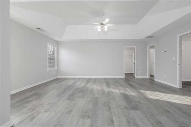 empty room featuring visible vents, baseboards, a raised ceiling, ceiling fan, and wood finished floors