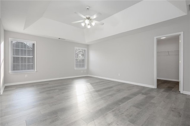 unfurnished bedroom with baseboards, wood finished floors, a spacious closet, a tray ceiling, and a closet