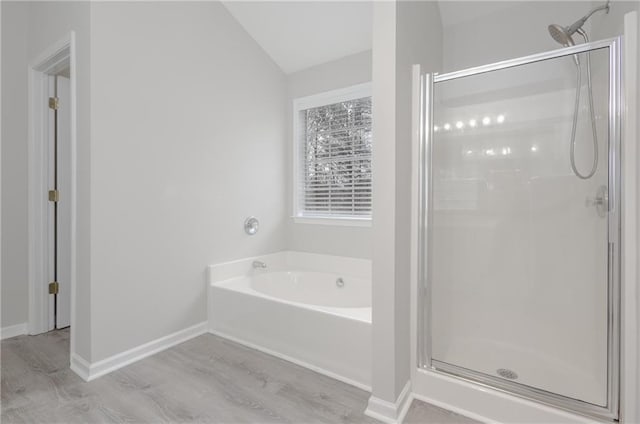 full bathroom featuring a stall shower, wood finished floors, a bath, and baseboards