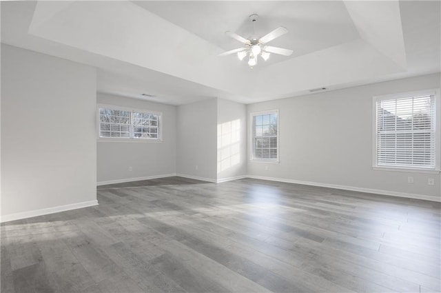 empty room featuring a tray ceiling, wood finished floors, a ceiling fan, and baseboards