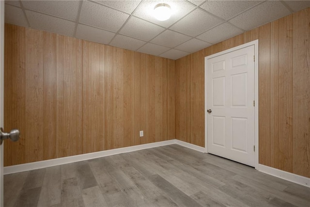 empty room with wooden walls, baseboards, a drop ceiling, and wood finished floors