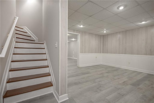 finished basement featuring stairway, a drop ceiling, and wood finished floors