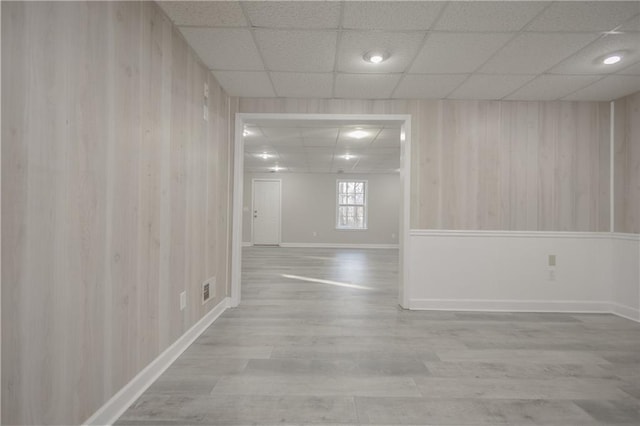 unfurnished room featuring wooden walls, baseboards, visible vents, a drop ceiling, and wood finished floors