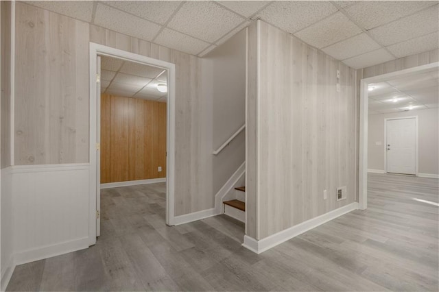 basement with stairs, a paneled ceiling, wooden walls, and wood finished floors