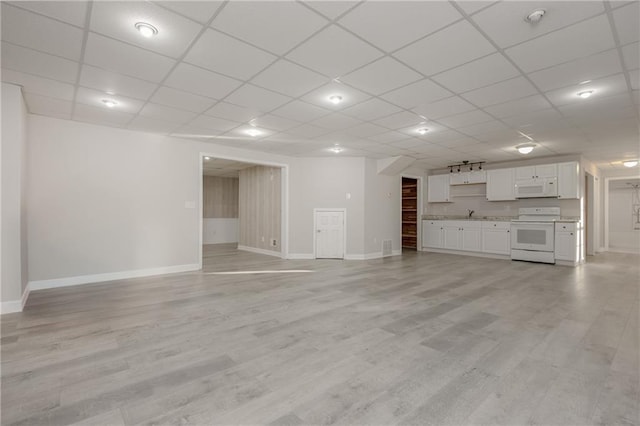 unfurnished living room featuring baseboards, a drop ceiling, and light wood finished floors