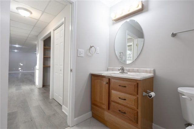 bathroom with a drop ceiling, vanity, toilet, and baseboards