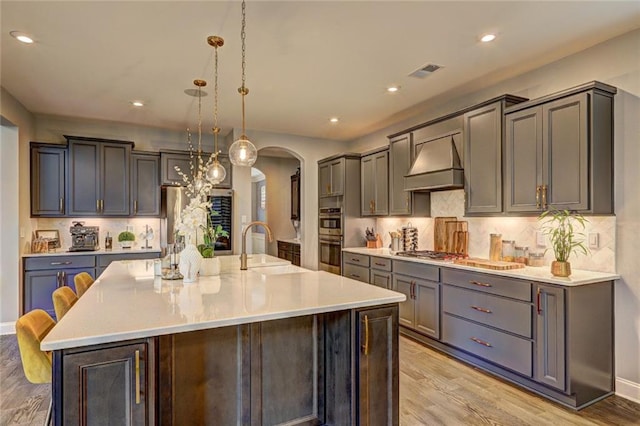13 Clearwater Ct, Hoschton, GA 30548 - kitchen with custom exhaust hood, arched walkways, stainless steel appliances, light wood finished floors, and backsplash