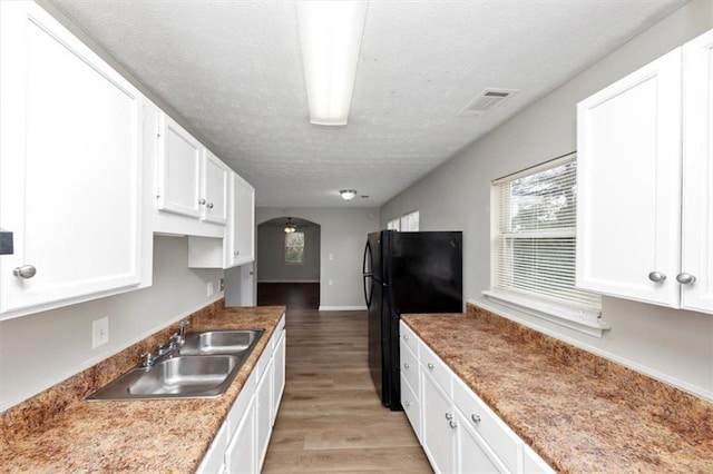 kitchen featuring freestanding refrigerator, light wood-style floors, white cabinets, a textured ceiling, and a sink