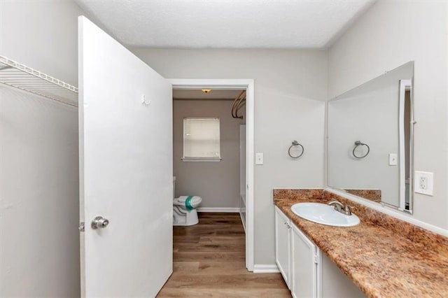 bathroom featuring baseboards, toilet, wood finished floors, and vanity