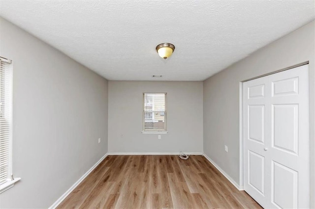 unfurnished bedroom featuring light wood-style flooring, visible vents, baseboards, and a textured ceiling