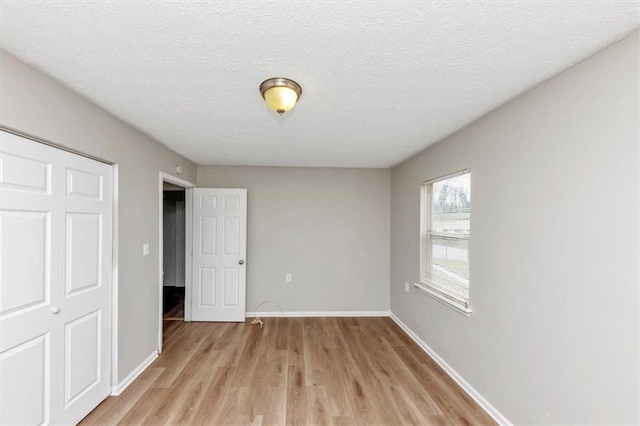 unfurnished bedroom featuring light wood-style flooring, a textured ceiling, and baseboards