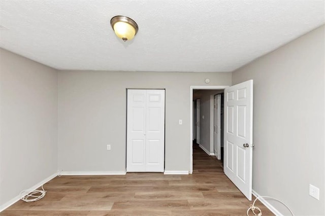 unfurnished bedroom with a closet, baseboards, a textured ceiling, and light wood finished floors