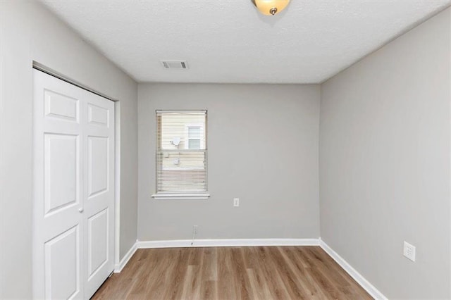 unfurnished bedroom featuring visible vents, a textured ceiling, light wood-type flooring, and baseboards