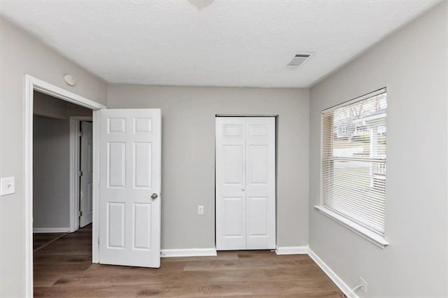 unfurnished bedroom with visible vents, baseboards, wood finished floors, a closet, and a textured ceiling