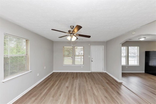 unfurnished living room with arched walkways, baseboards, a ceiling fan, and wood finished floors