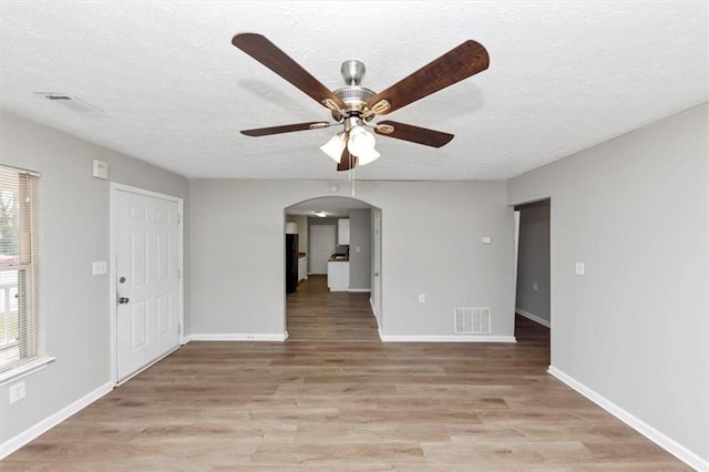 unfurnished living room with arched walkways, visible vents, light wood-style flooring, and ceiling fan