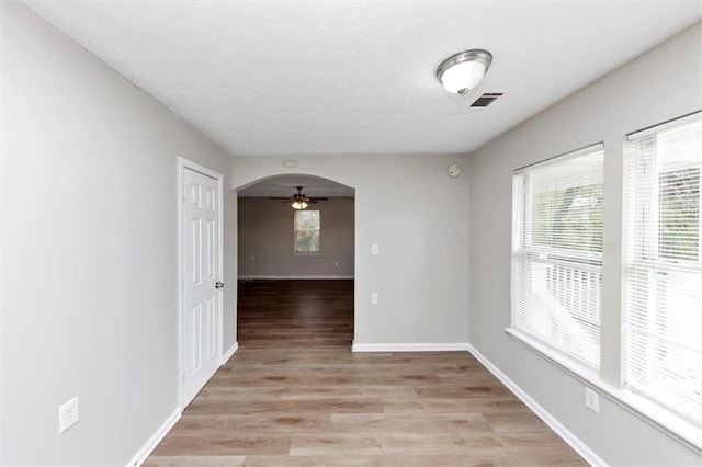 empty room featuring baseboards, plenty of natural light, ceiling fan, and light wood finished floors