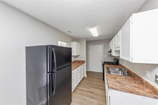 kitchen featuring a sink, gas range oven, freestanding refrigerator, white cabinets, and light wood finished floors