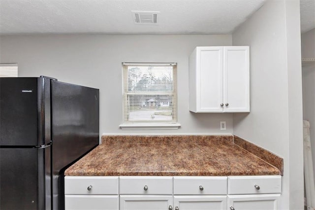 kitchen with visible vents, a textured ceiling, dark countertops, freestanding refrigerator, and white cabinets