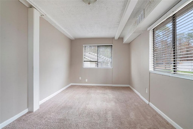 carpeted empty room featuring beamed ceiling, a textured ceiling, and a wealth of natural light