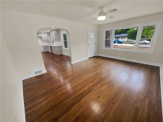 unfurnished living room featuring dark wood-style floors, visible vents, baseboards, arched walkways, and ceiling fan