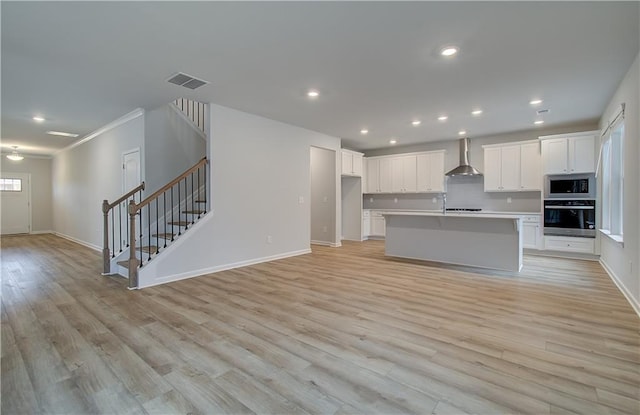 kitchen featuring wall chimney range hood, white cabinets, appliances with stainless steel finishes, and visible vents