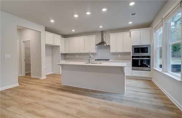 kitchen with light wood-type flooring, a sink, visible vents, appliances with stainless steel finishes, and wall chimney exhaust hood