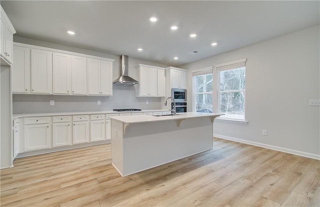 kitchen featuring white cabinetry, light wood-style flooring, light countertops, and wall chimney range hood