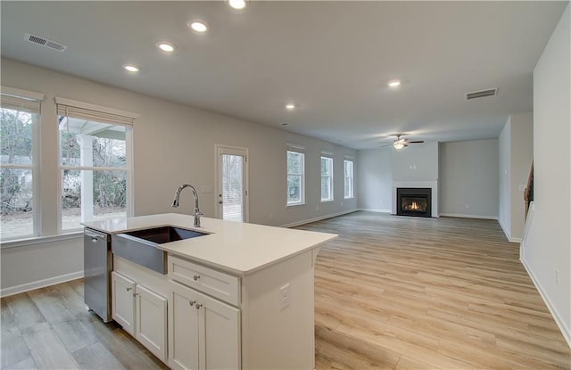kitchen featuring visible vents, dishwasher, a ceiling fan, a sink, and a glass covered fireplace