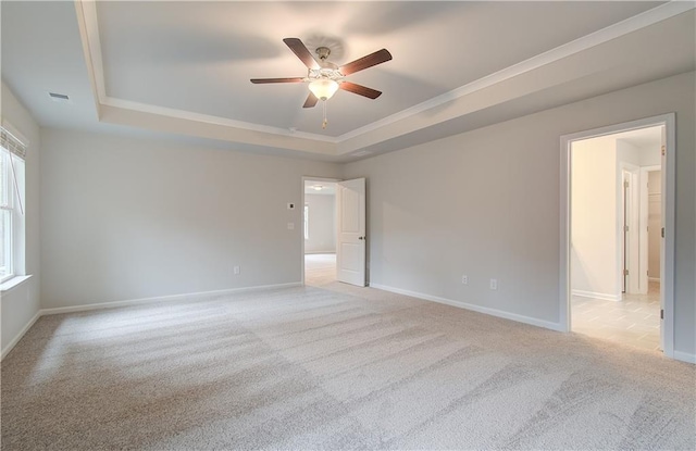 spare room featuring a tray ceiling, crown molding, light carpet, baseboards, and ceiling fan