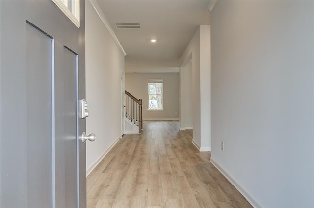 corridor featuring stairway, light wood-style flooring, baseboards, visible vents, and ornamental molding