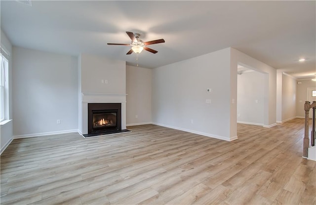 unfurnished living room featuring a ceiling fan, a glass covered fireplace, baseboards, and light wood-type flooring