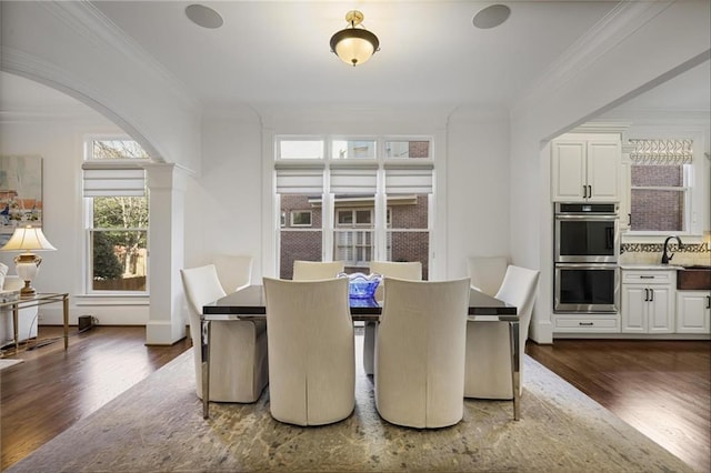 dining area featuring dark wood-type flooring, ornamental molding, and ornate columns