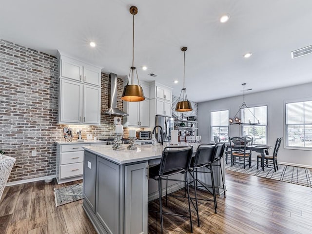 kitchen featuring a kitchen island with sink, white cabinets, wall chimney range hood, hanging light fixtures, and dark hardwood / wood-style floors