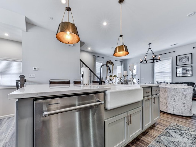 kitchen featuring gray cabinetry, stainless steel dishwasher, an island with sink, decorative light fixtures, and light wood-type flooring