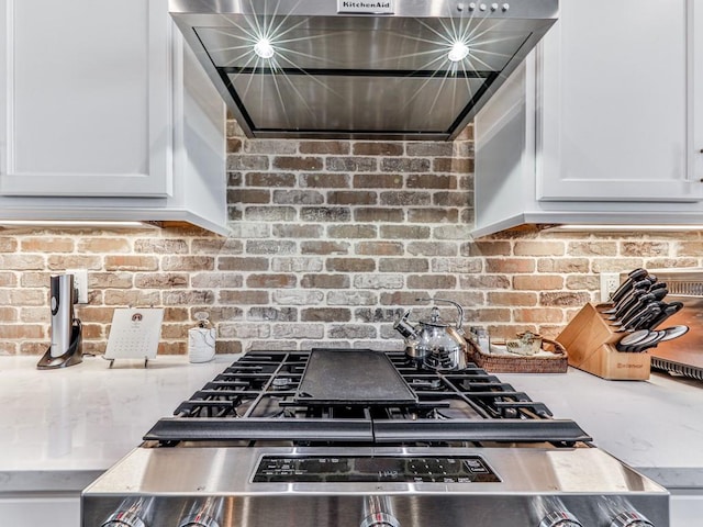 kitchen with white cabinets, stainless steel range oven, and brick wall