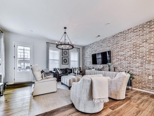 living room with hardwood / wood-style floors, a chandelier, and brick wall