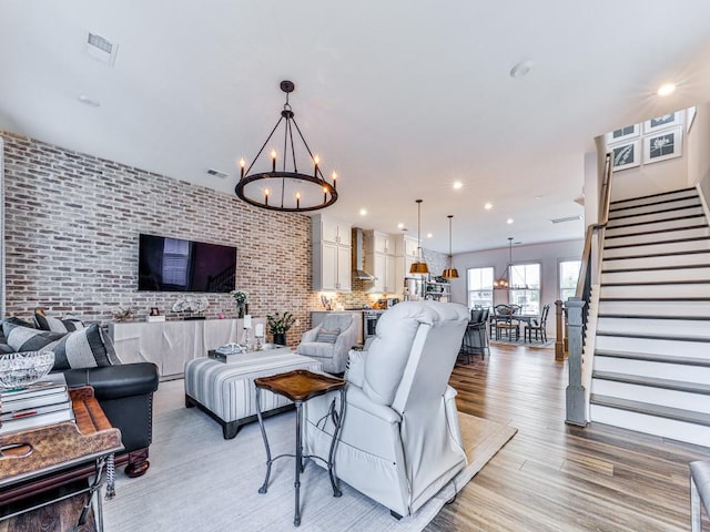 living room with light wood-type flooring, brick wall, and a notable chandelier