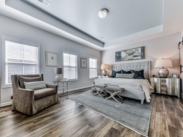 bedroom with a barn door, a raised ceiling, and dark wood-type flooring