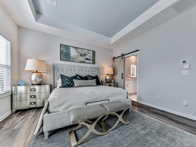 bedroom featuring a raised ceiling, ensuite bath, dark hardwood / wood-style flooring, and a barn door