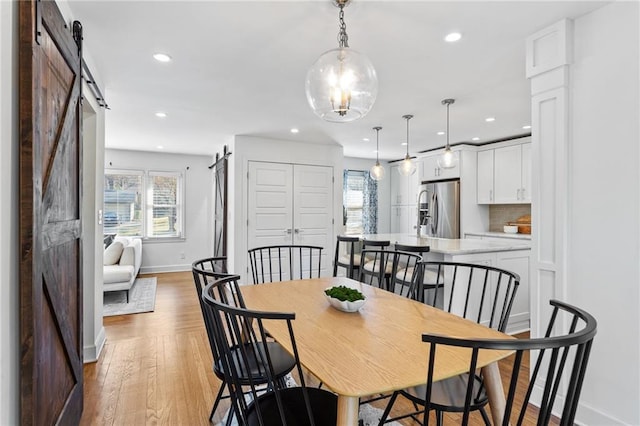 dining room with a barn door, recessed lighting, baseboards, and light wood finished floors