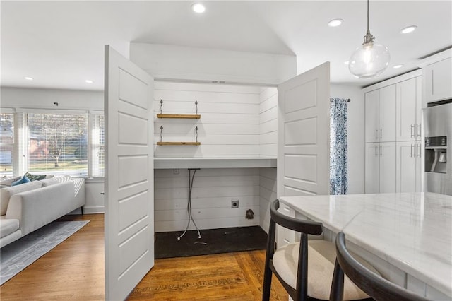 kitchen with light stone counters, dark wood-style flooring, white cabinetry, a kitchen breakfast bar, and stainless steel fridge