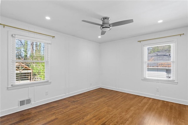 spare room with a ceiling fan, a decorative wall, wood finished floors, and visible vents