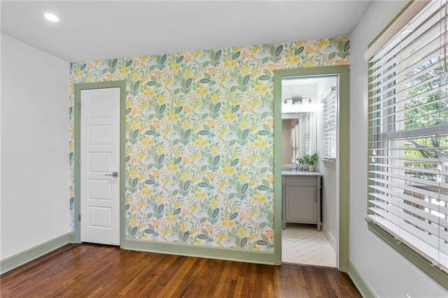 empty room featuring baseboards, wood finished floors, and wallpapered walls