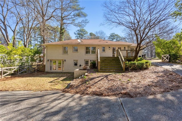 view of front facade with fence, stairway, a wooden deck, stucco siding, and french doors