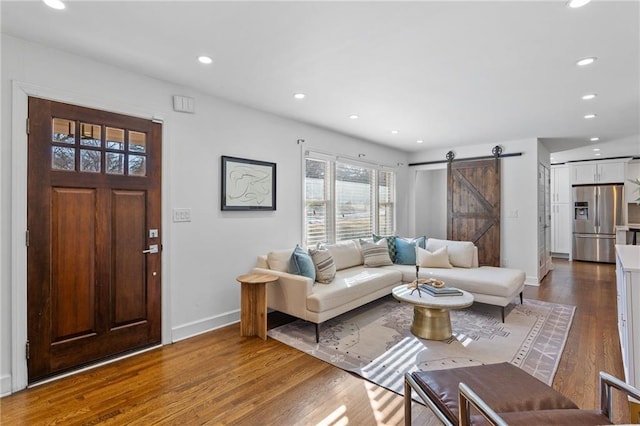 living area with a barn door, recessed lighting, dark wood-type flooring, and baseboards