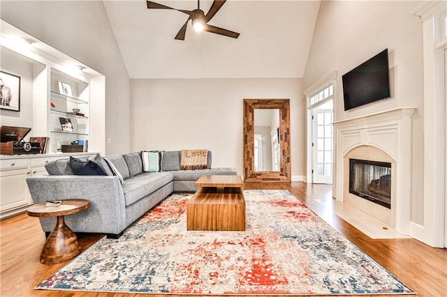 living room featuring high vaulted ceiling, a ceiling fan, wood finished floors, a premium fireplace, and baseboards